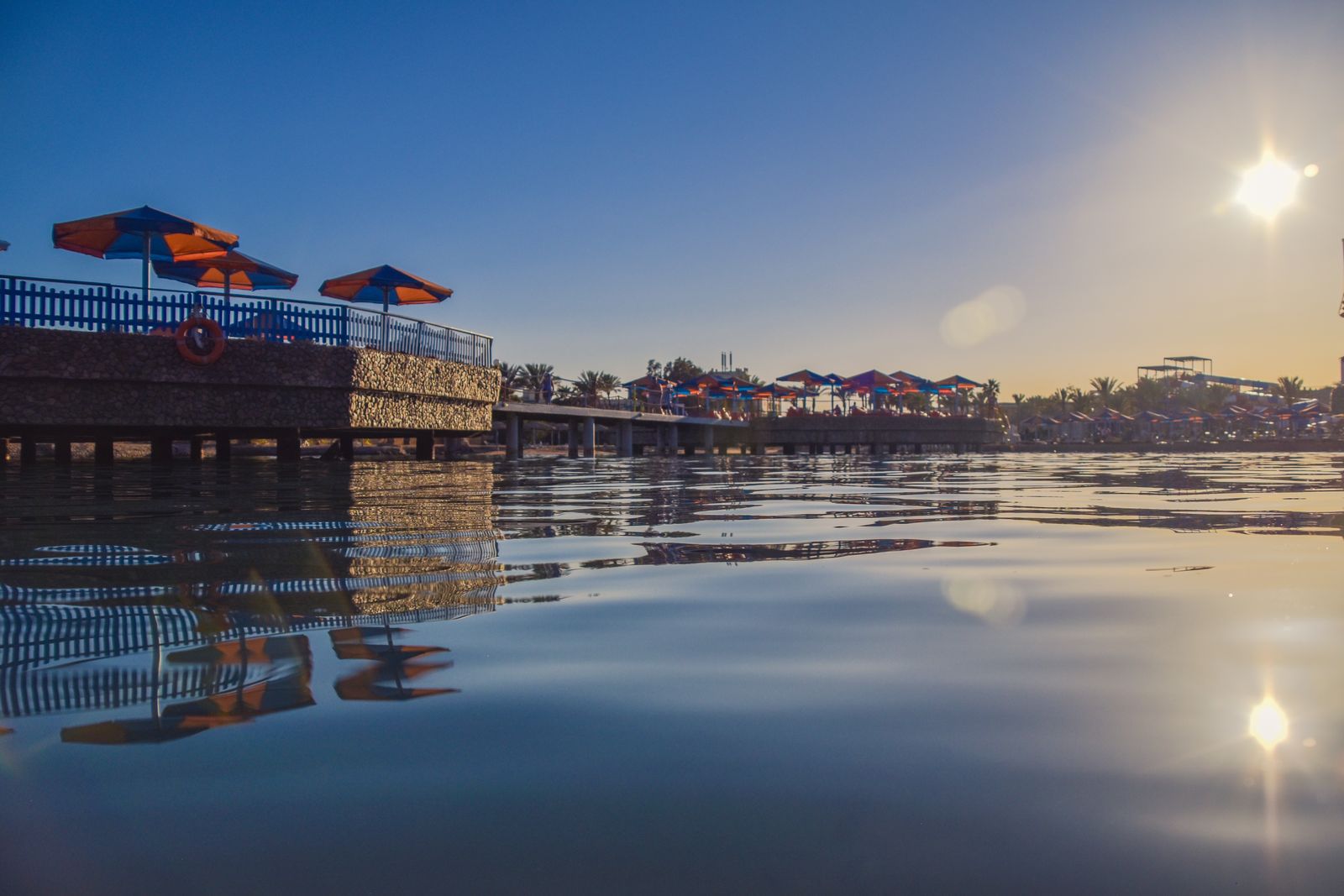 Wooden piers with sun umbrellas on the Hurghada waterfront, reflected in calm water at sunrise